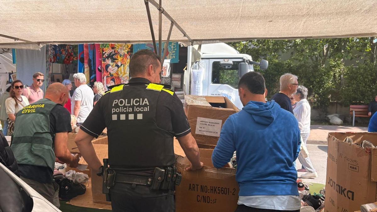Els agents requisant diversos objectes falsificats en una de les parades del mercat setmanal de Palamós.