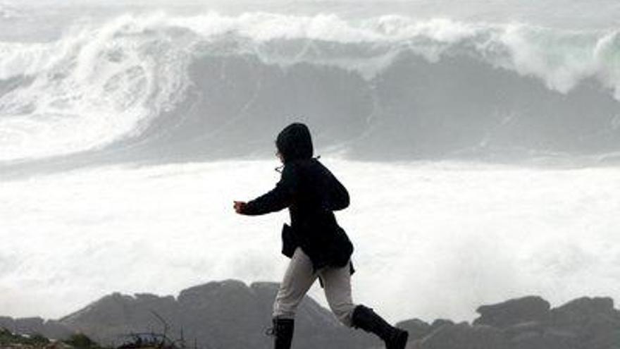 Una persona corre por Corrubedo (Riveira) en busca de un refugio contra la lluvia mientras el temporal que azota las costas gallegas sigue provocando fuertes oleajes.