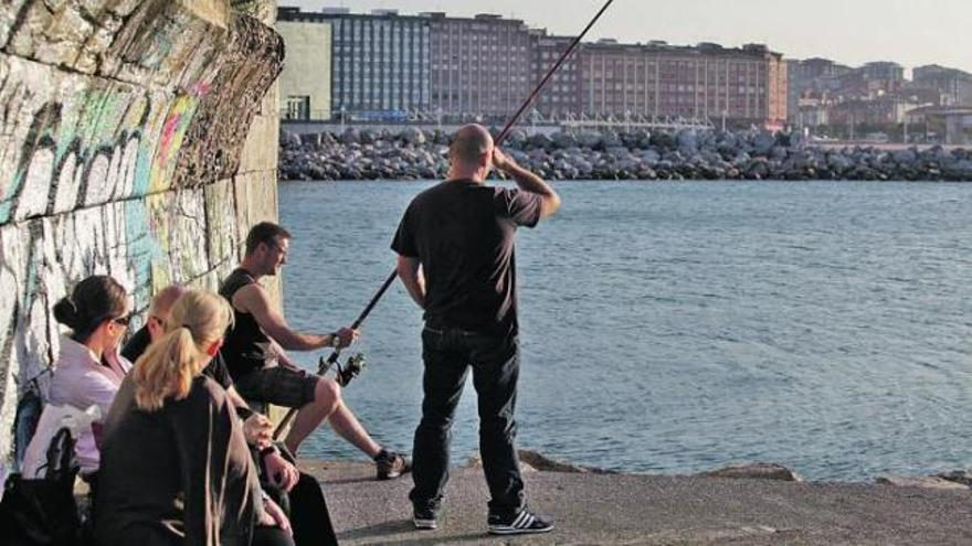 Un aficionado pesca en el puerto deportivo de Gijón. A la derecha, José Díaz Jove.