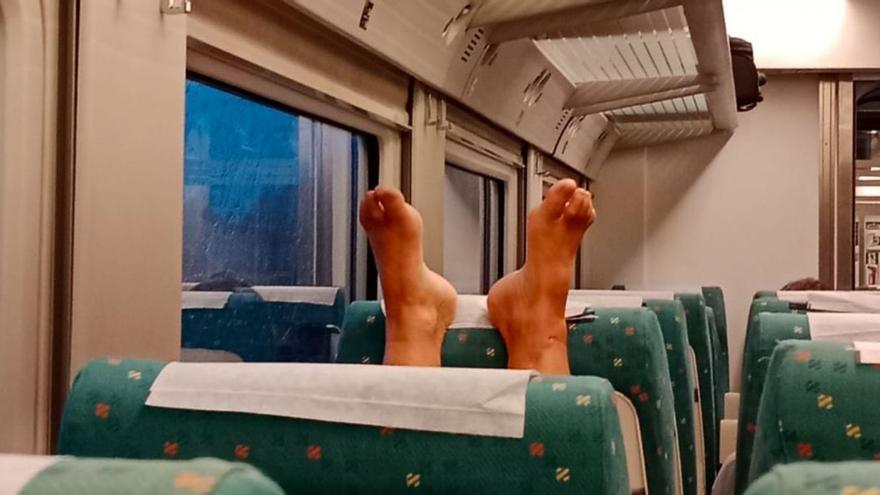 Un viajero reposa los pies sobre el cabezal del asiento de delante.