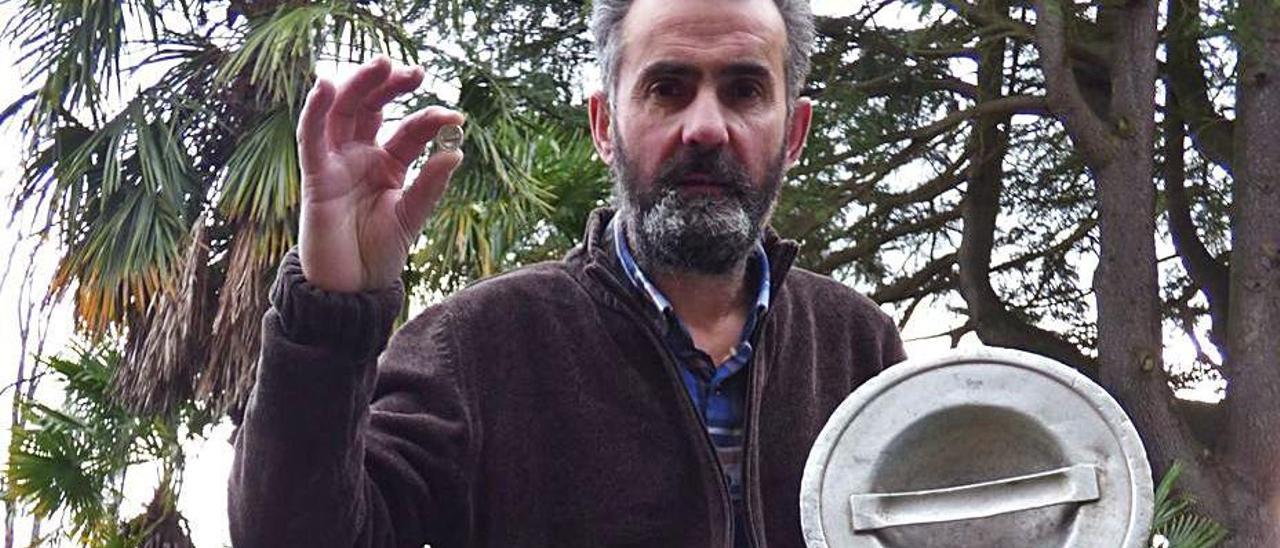 Lucas Santiago, tras antiguos bidones de leche, muestra en su mano la réplica en joya de la tapa. | D. Á.