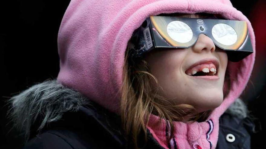 A la izquierda, dos niños observan el eclipse con gafas especiales en el Reino Unido. A la derecha, el eclipse, sobre una mezquita en Oxford.