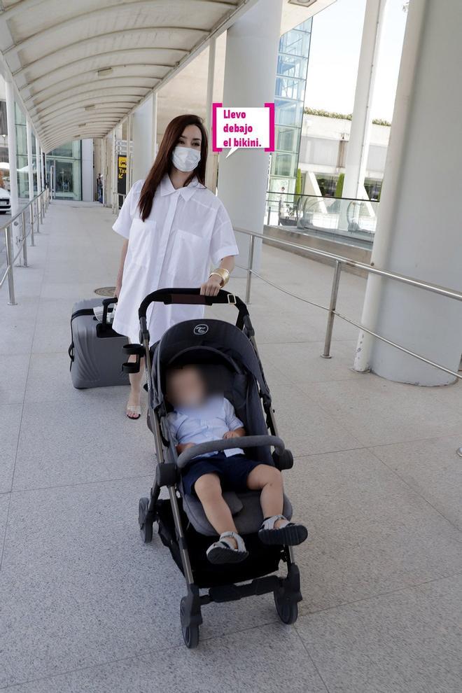 Adara Molinero con vestido blanco, maleta, mascarilla y el carrito con el bebé