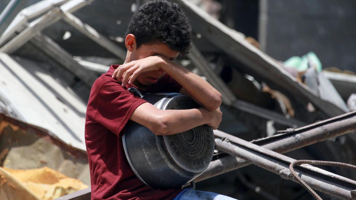 Un niño gesticula mientras palestinos desplazados recogen porciones de comida cocinada en una distribución benéfica en Jabalia, en el norte de la Franja de Gaza, el 19 de mayo de 2025.