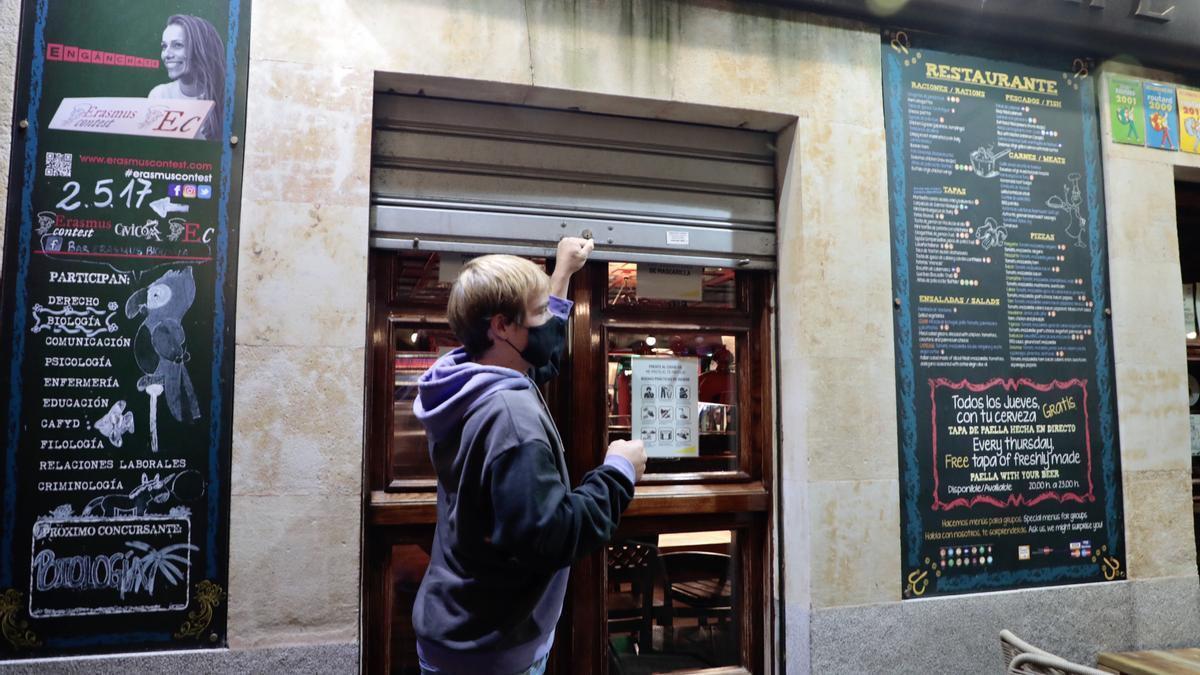 Un hombre cierra la persiana de su establecimiento en Salamanca.
