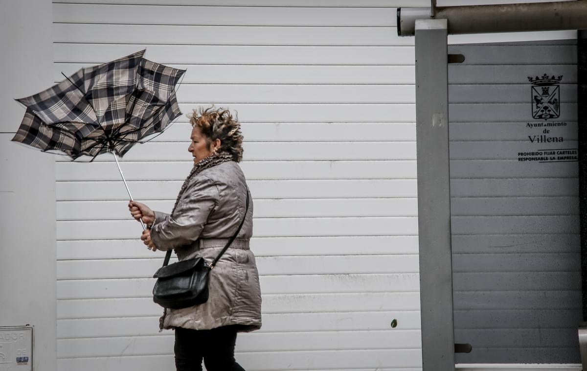 Una mujer de Villena luchando contra el viento para que no le arrebate el paraguas.