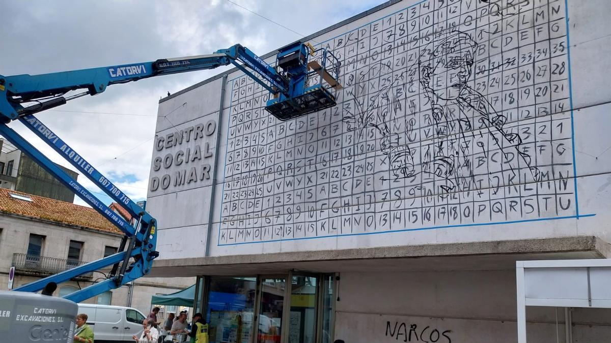La artista Mariana Duarte, en la grúa, trabajando en el mural sobre la fachada del Centro Social do Mar de Bueu.