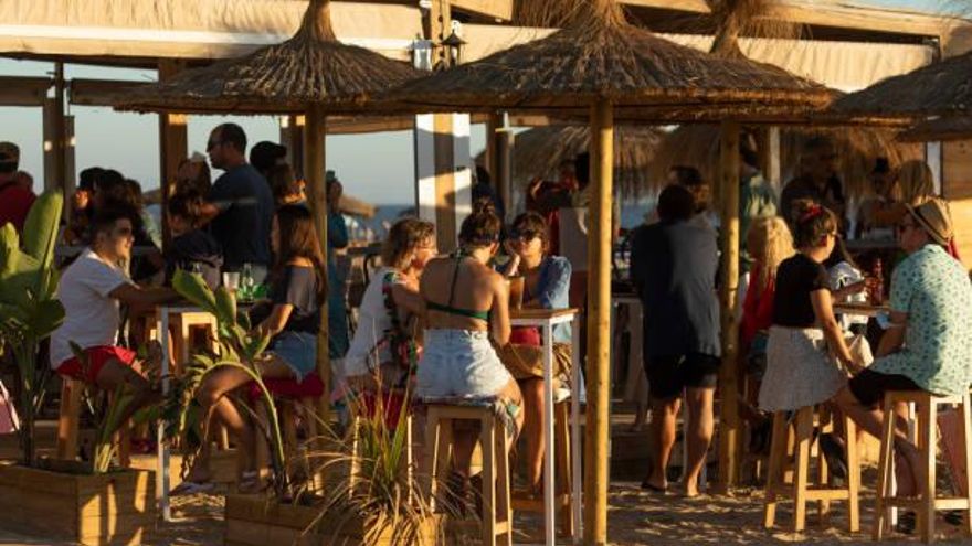 Terraza de un chiringuito con personas tomando copas mientras atardece.