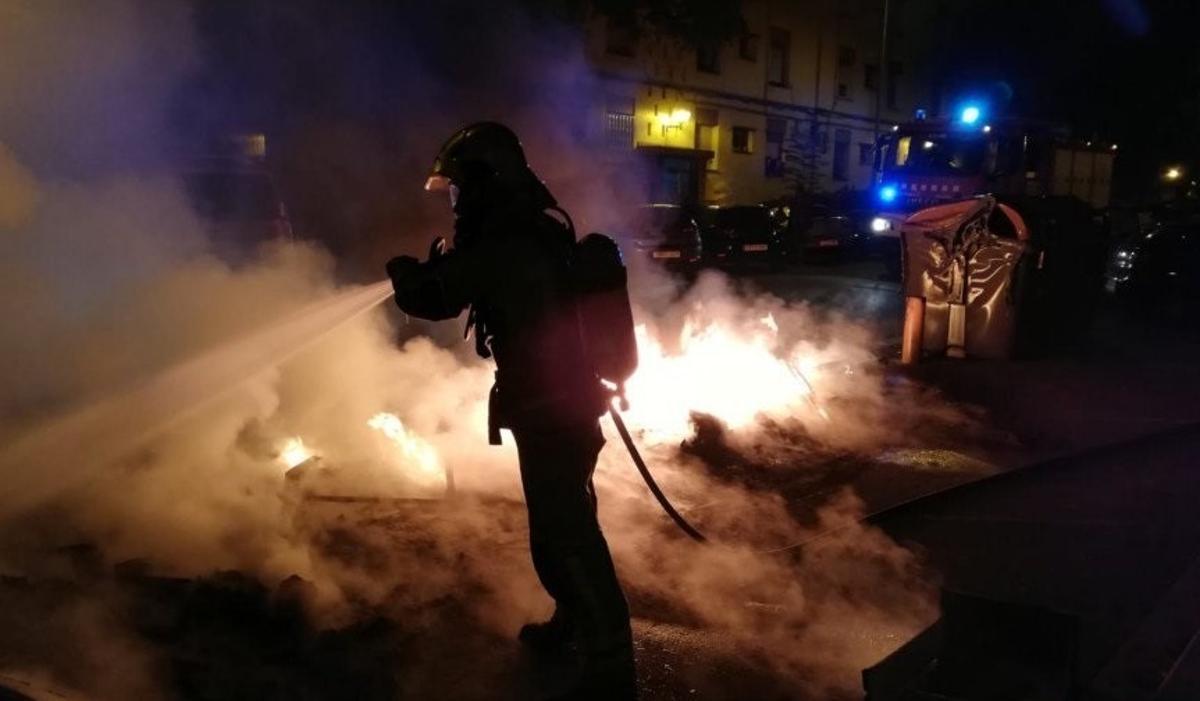 Un bombero apaga un incendio en Sabadell que afectó a varios contenedores.