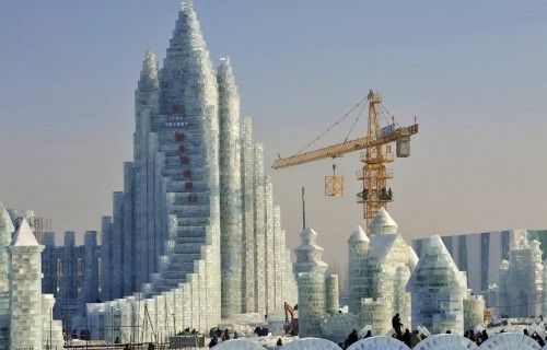 Workers and a crane are seen next to a newly-built ice sculpture of a castle ahead of the 30th Harbin Ice and Snow Festival, in Harbin