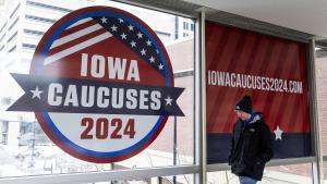 Un joven camina frente a un cartel de los caucus de Iowa, en Des Moines (Estados Unidos).