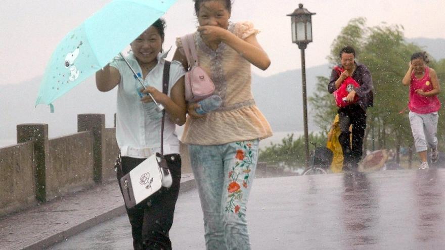 Chinos caminan entre la lluvia provocada por un tifón. EFE/Zhu Yinwei