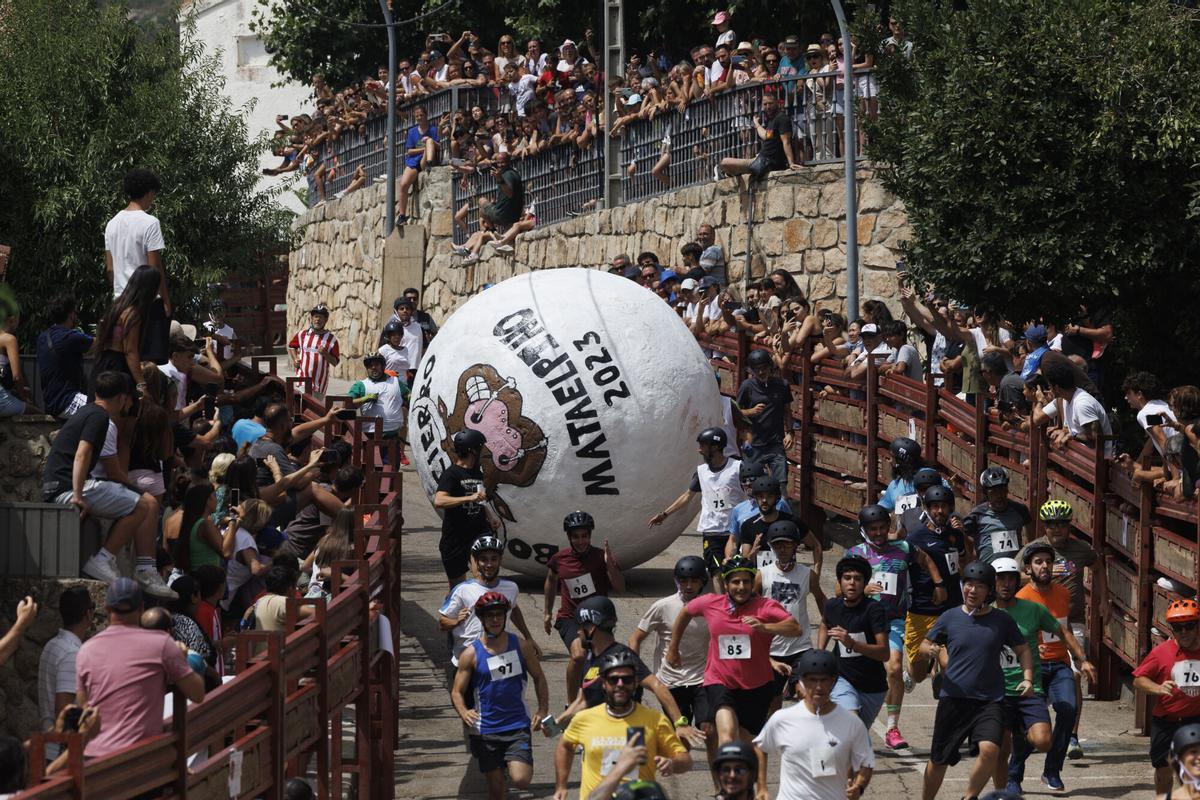MATAELPINO (MADRID), 26/08/2023.- Un grupo de personas corren delante de una esfera, fabricada en poliestireno expandido, de 3 metros de diámetro y más de 200kg de peso, en el tradicional "boloencierro" paraadultos, durante las fiesta patronales en honor a San Bartolomé en Mataelpino, (Madrid) este sábado. EFE/Sergio Pérez
