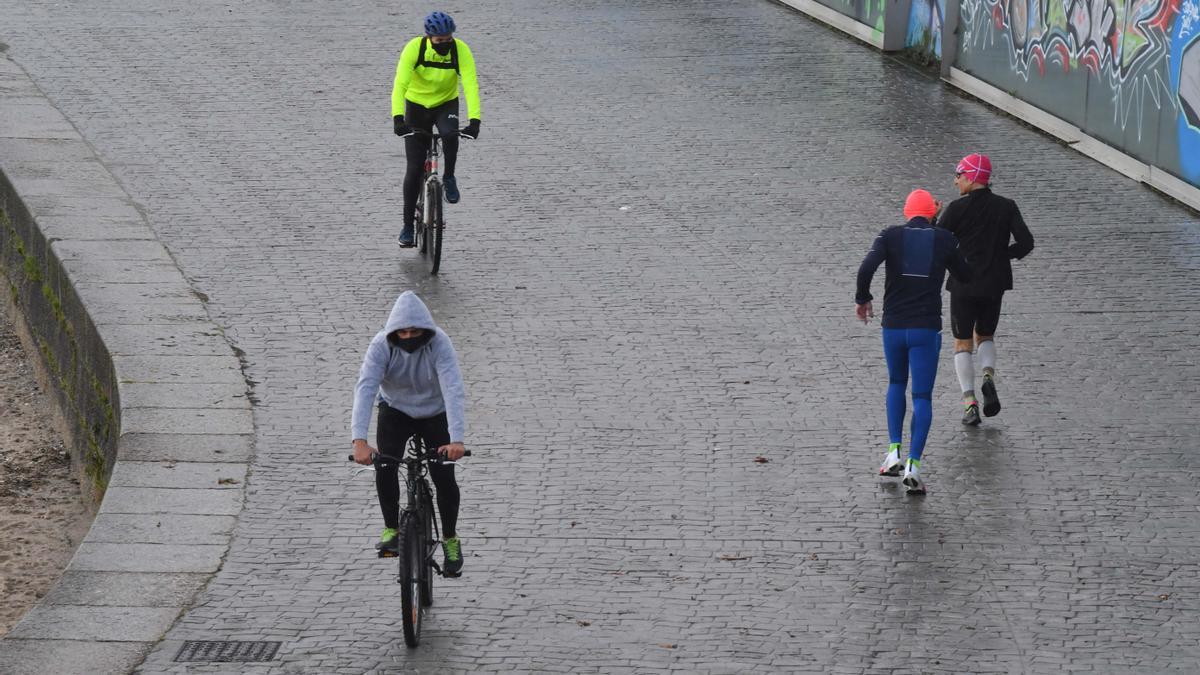 Varias personas abrigadas con capucha practican deporte en el andén de Riazor.