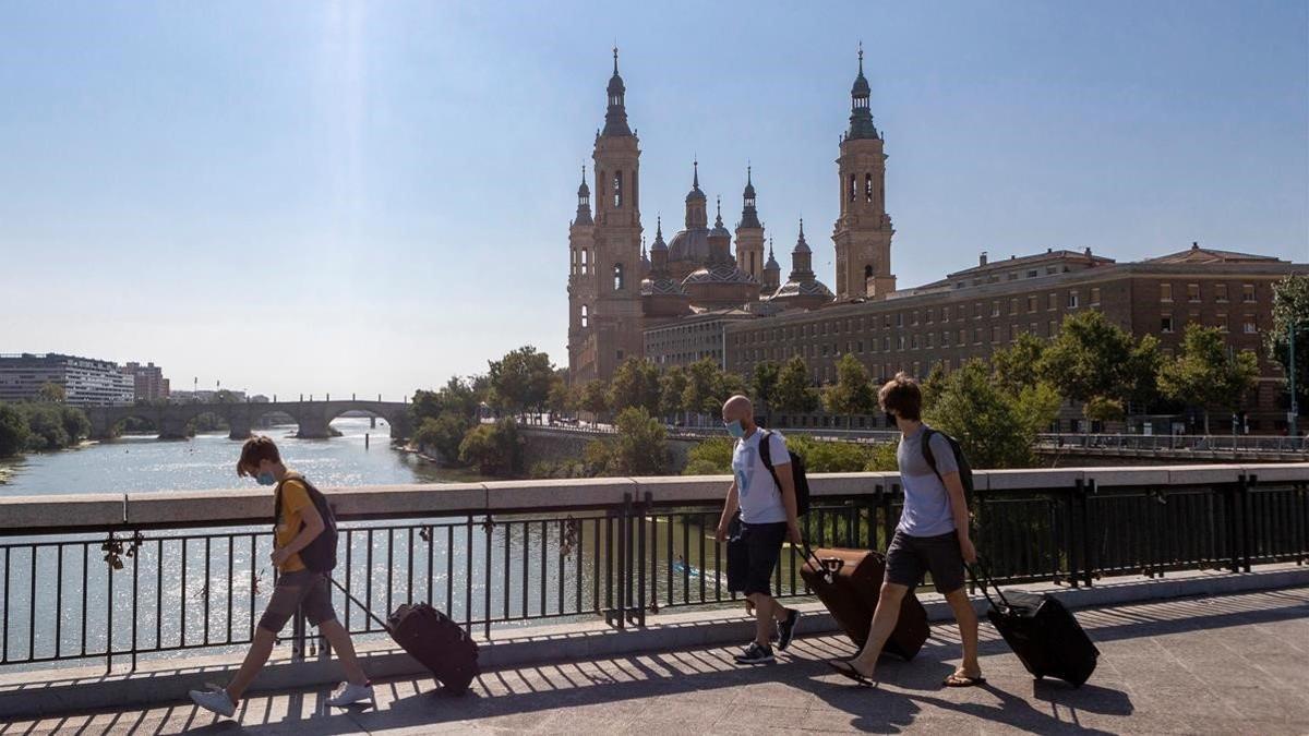 Personas con maletas cruzan el Puente de Santiago de Zaragoza, el 15 de agosto del 2020