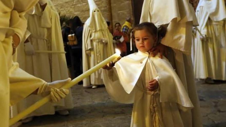 Un cofrade enciende el pequeño cirio de un niño.