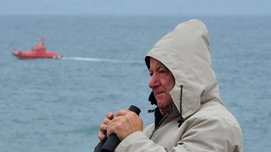 Un vecino observa la costa y al fondo una lancha de búsqueda. // I.A.