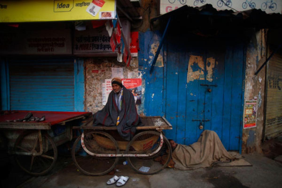Dos homes dormen, abrigats amb una manta, davant d’una botiga tancada durant un fred matí a Nova Delhi (Índia).