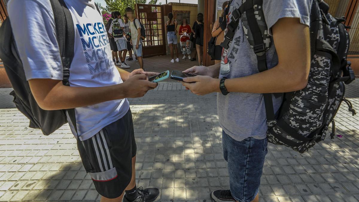 Adolescentes con sus teléfonos móviles, frente a un instituto