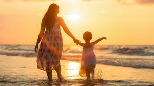 Una madre lleva de la mano a su hija en una playa.