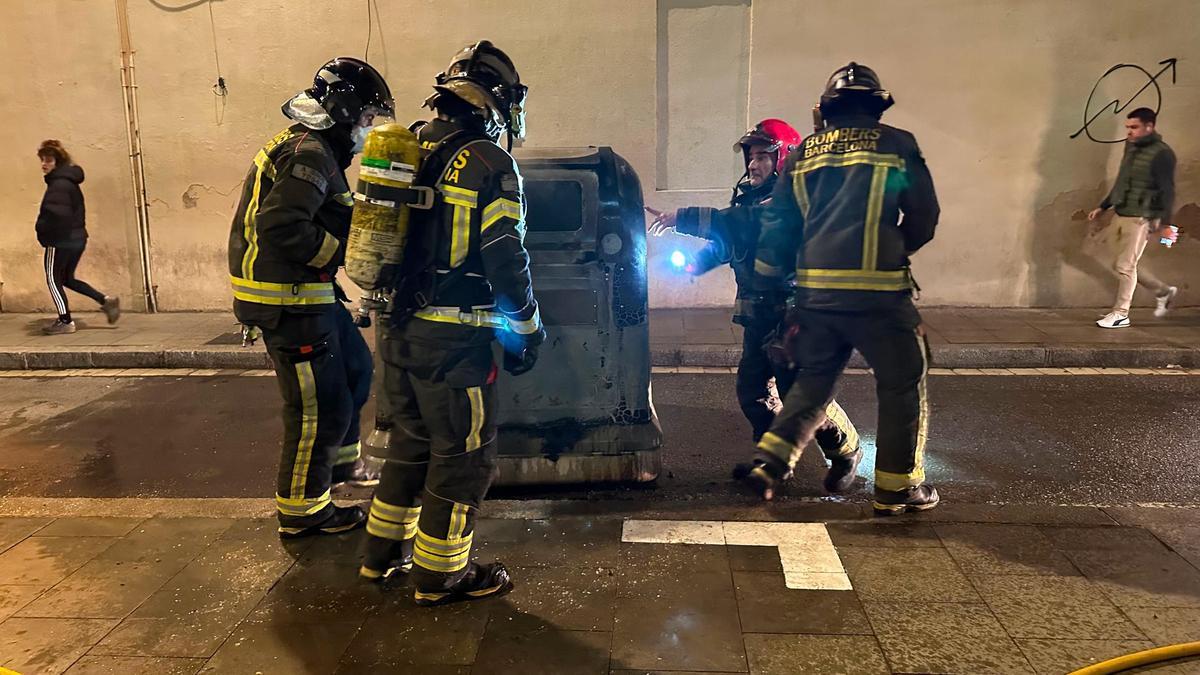 Los Bombers inspeccionan un contenedor quemado en el barrio de Gràcia.