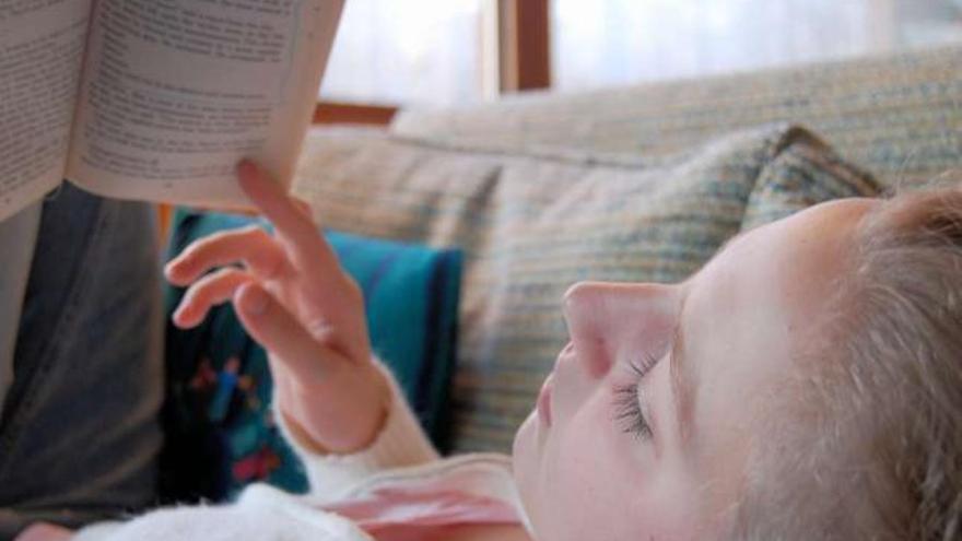 Una niña tumbada en un sofá con un libro abierto. / l. o.