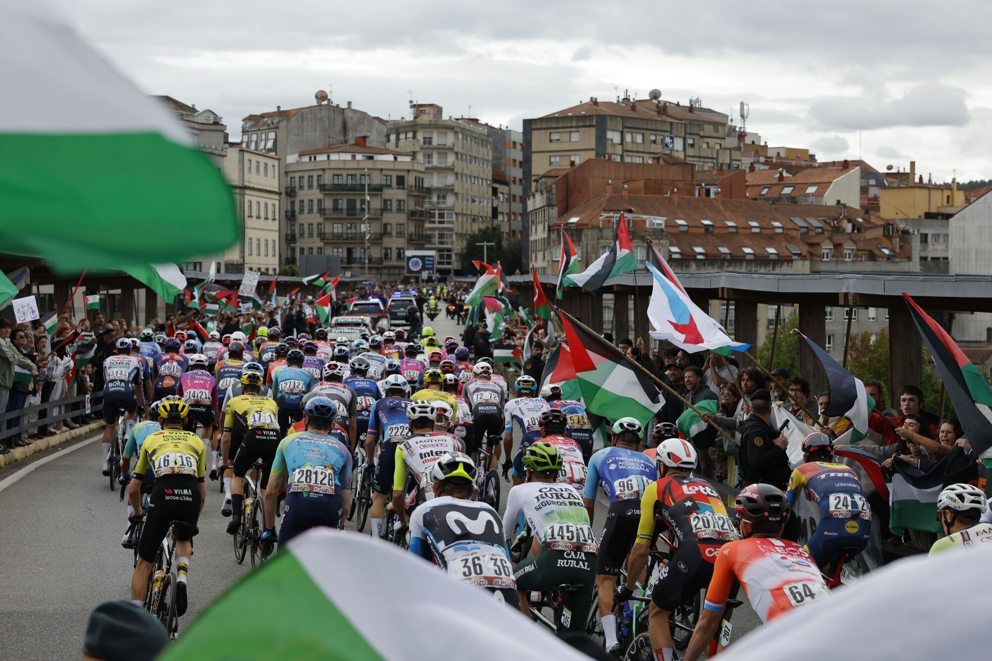 POIO (PONTEVEDRA), 09/09/2025.-El pelotón pasa ante las personas concentradas en protesta por la situación de Gaza , al inicio de la etapa 16 de la Vuelta Ciclista a España que se disputa este martes entre Poio y Mos-Castro de Herville (Pontevedra), de 167.9 km de recorrido. EFE/Lavandeira