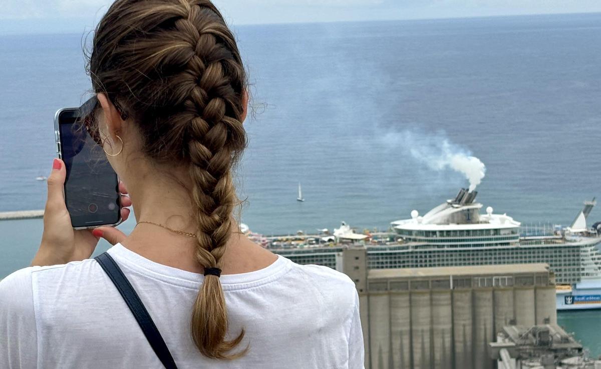 Una turista fotografia Barcelona desde el castillo de Montjuïc, con un humeante crucero a sus pies, este domingo