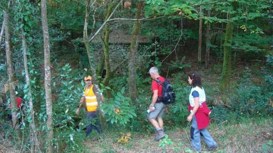 Varios excursionistas caminan ante uno de los molinos del sendero circular de Couso.  // IEM