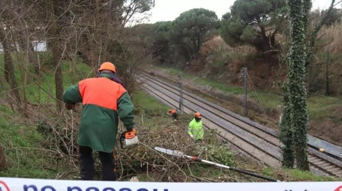 Técnicos de Adif trabajando en una franja de tierra junto a las vías de Rodalies.