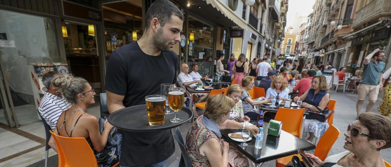 Un camarero atiende la terraza de un bar, a pleno rendimiento, en el centro.