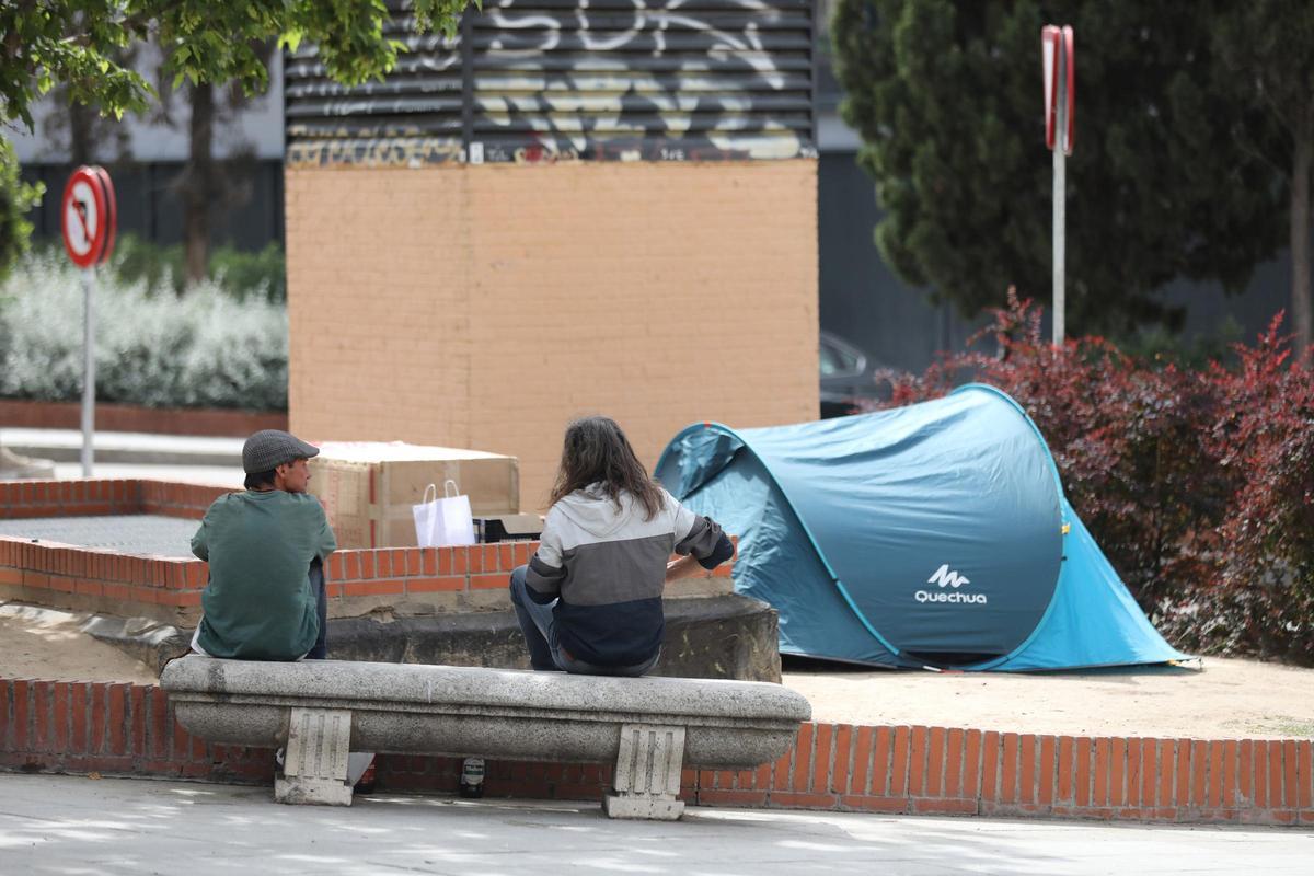 Varias personas sintecho junto a una tienda de campaña, en la calle.