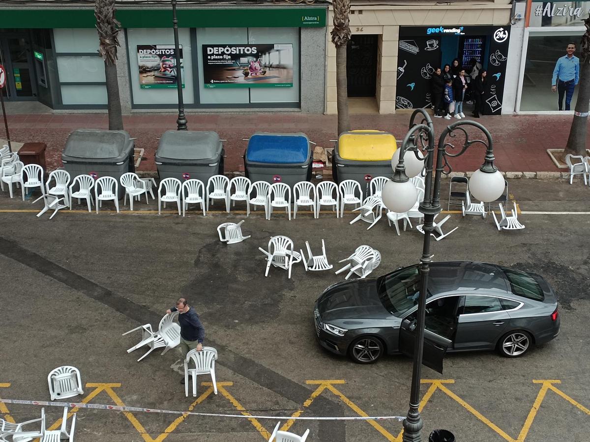 Un conductor retira sillas que el viento ha arrastrado al medio de calle.