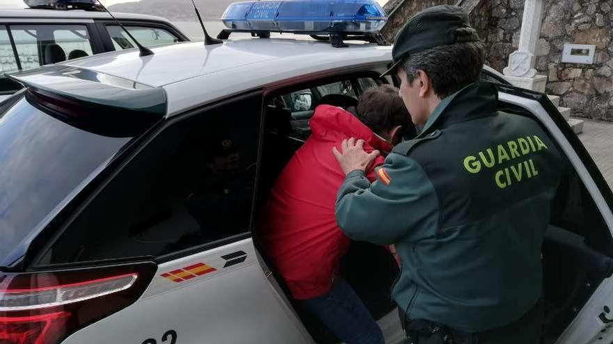 Un agente introduce a J.F.O.S., vecino de Oia de 47 años en el coche tras la detención. // Guardia Civil