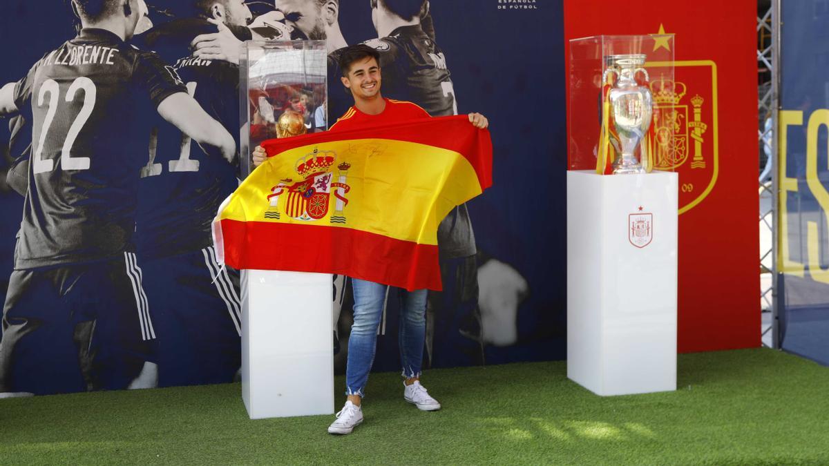 Un aficionado posa con una bandera de España y los trofeos de la selección