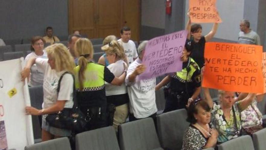 Dos agentes desalojan a los vecinos mientras muestran pancartas contra el PP y denunciando los malos olores que sufren.