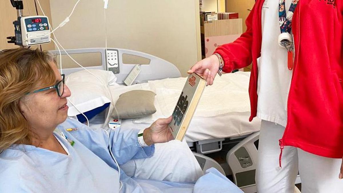 Una profesional del Hospital del Vinalopó entrega un libro a una paciente ingresada.