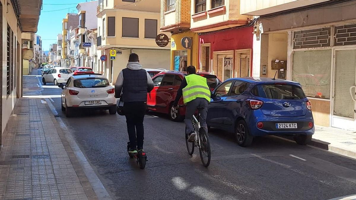 Dos vehículos de movilidad personal, un patinete eléctrico y una bicicleta, circulan por la calle Crist de la Penitència de Vila-real.