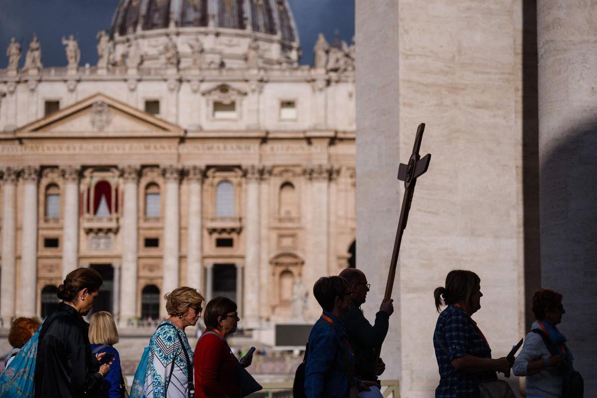 Faithful walk with a cross with the St Peters Basilica in the background a day prior to the start of the conclave, at the Vatican on May 6, 2025. (Photo by Dimitar DILKOFF / AFP)