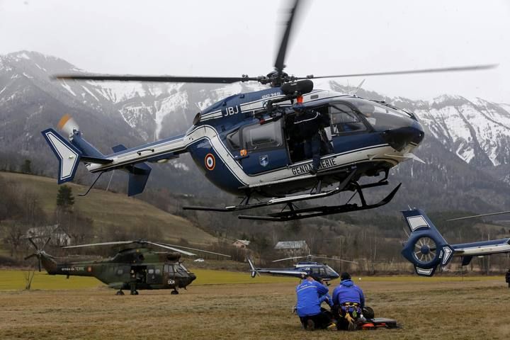 A French rescue helicopter from the French Gendarmerie hovers above a field where Alpine rescue forces gather in front of the French Alps during a rescue operation near the crash site of an Airbus A320