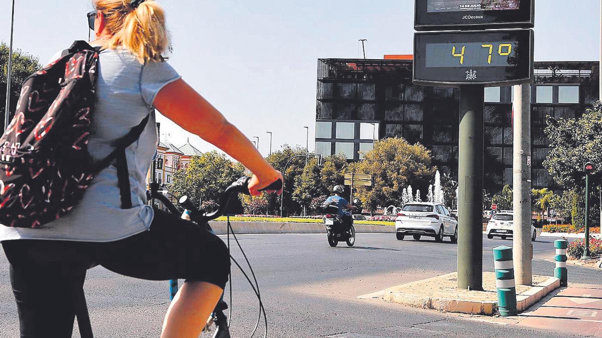 Una mujer en bicicleta ante un termómetro a 47 grados.