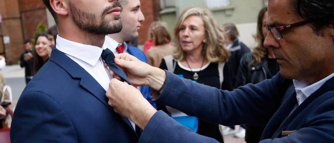 Un hombre coloca la corbata a un graduado.