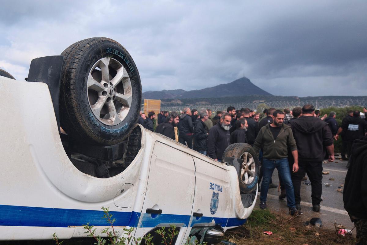 Farmers gather next to an overturned police vehicle during clashes with officers blocking their march to Chanias airport on Crete, Greece, Monday, Dec. 8, 2025, amid protests over delayed EU farm subsidies. (AP Photo/Giannis Angelakis)