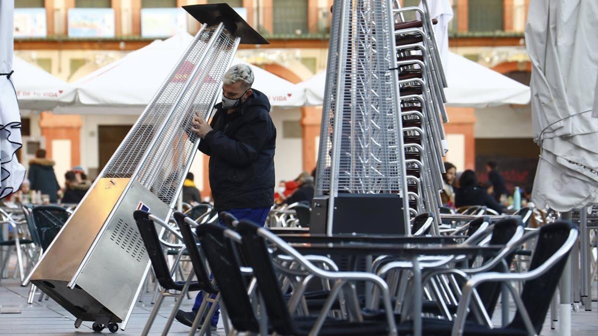 COR01  CORDOBA  11 01 2021 - Un trabajador recoge el mobiliario de la terraza de un restaurante en el centro de Cordoba  hoy lunes cuando han entrado en vigor las nuevas restricciones en Andalucia por el aumento de casos de la covid  entre ellas el cierre perimetral de la comunidad autonoma  el adelanto del cierre de la hosteleria  del toque de queda de las once a las diez de la noche y la limitacion de las reuniones a seis personas  estas medidas estaran vigentes hasta la medianoche del 24 al 25 de enero  EFE Salas