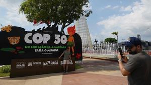 Un turista posa para una foto con el cartel del COP30 y su mascota, en Belém, Brasil.