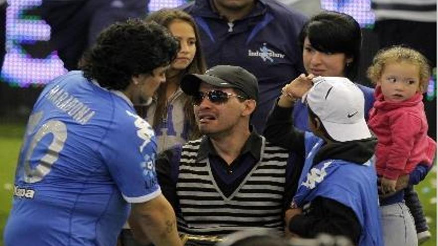 Cáceres, con gorra y gafas, rodeado por su familia, recibe el saludo de Maradona.