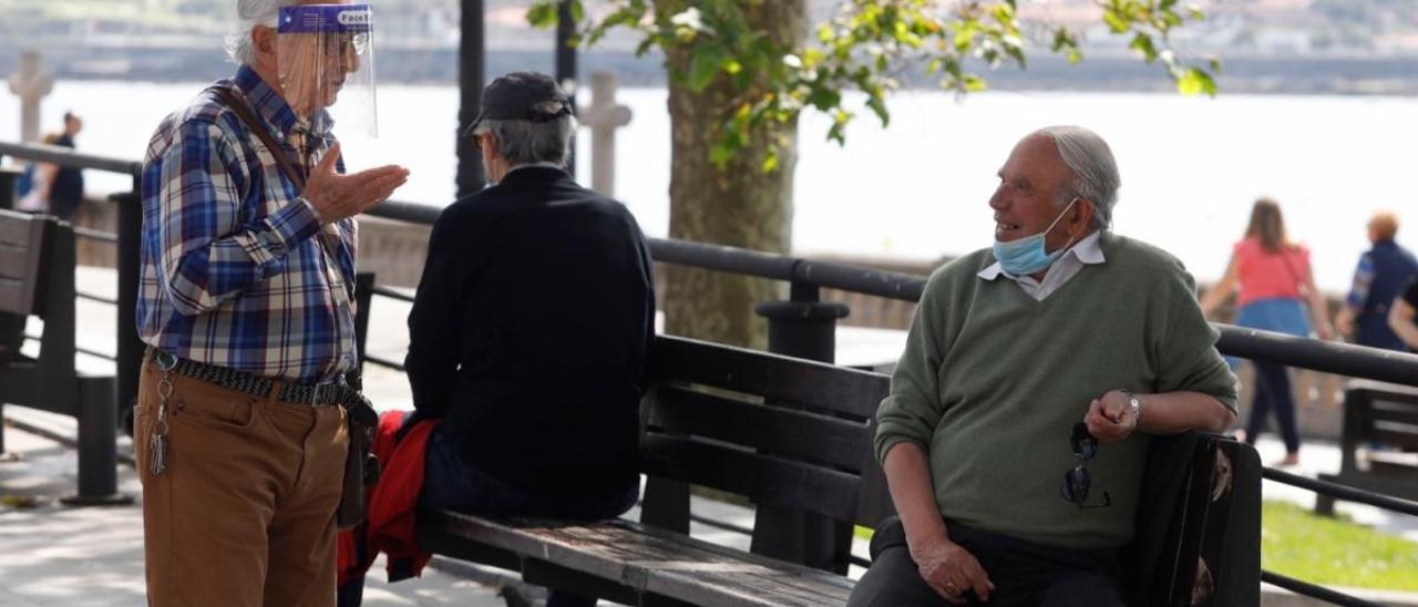 Un grupo de hombre habla en un banco en Gijón.