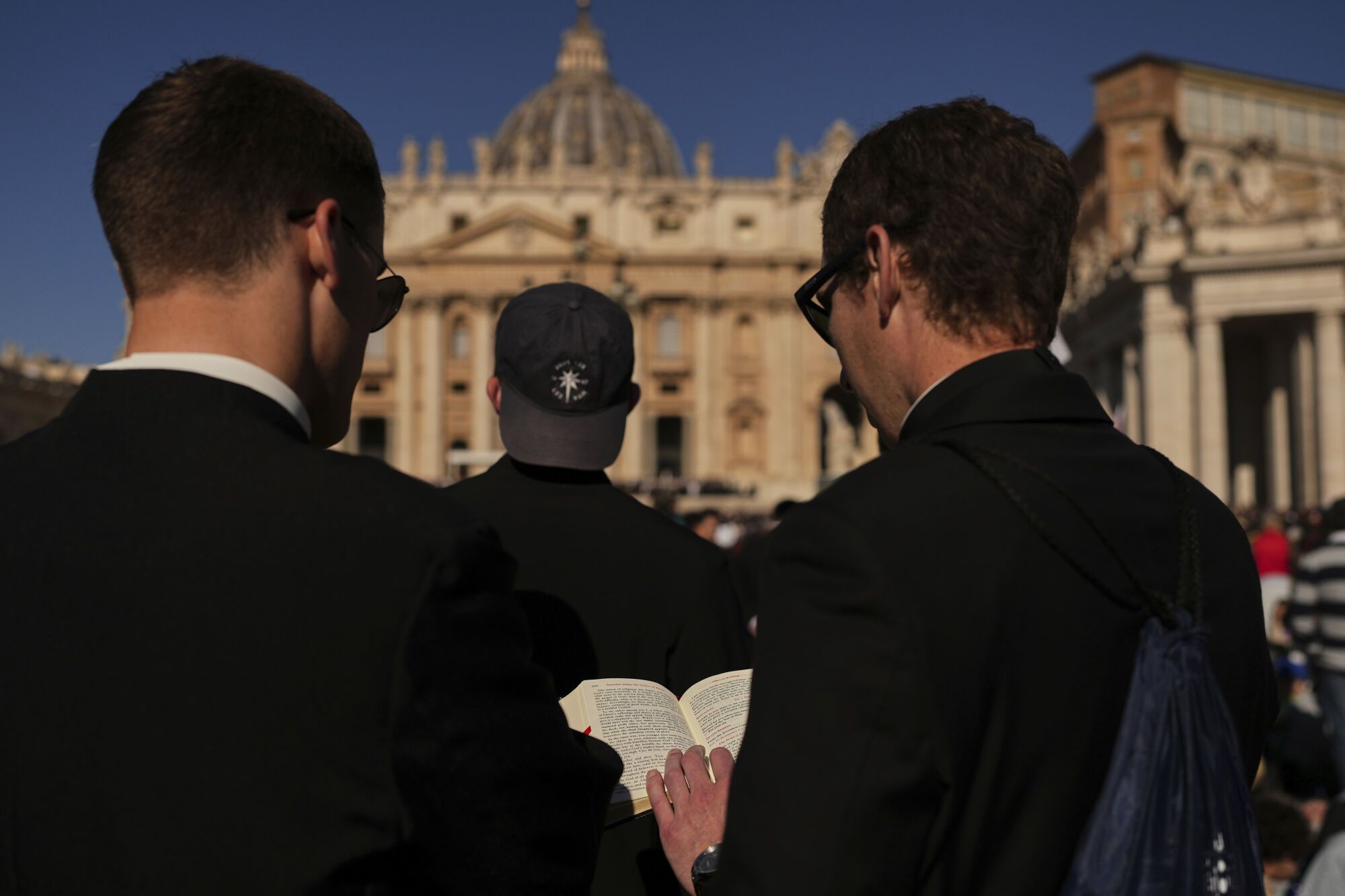 Men read from a religious book while waiting for the funeral of Pope Francis in St. Peter's Square at the Vatican, Saturday, April 26, 2025. (AP Photo/Andreea Alexandru). EDITORIAL USE ONLY/ONLY ITALY AND SPAIN