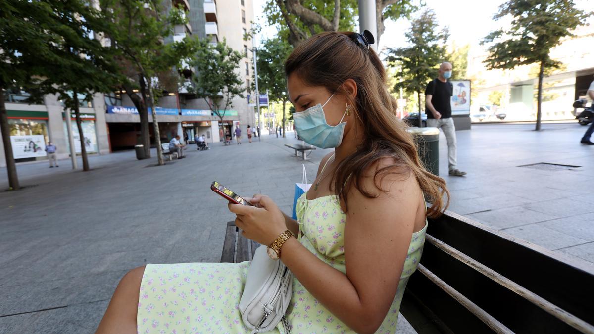 Una joven habla por Whatsapp sentada en un banco de la plaza Aragón de Zaragoza.