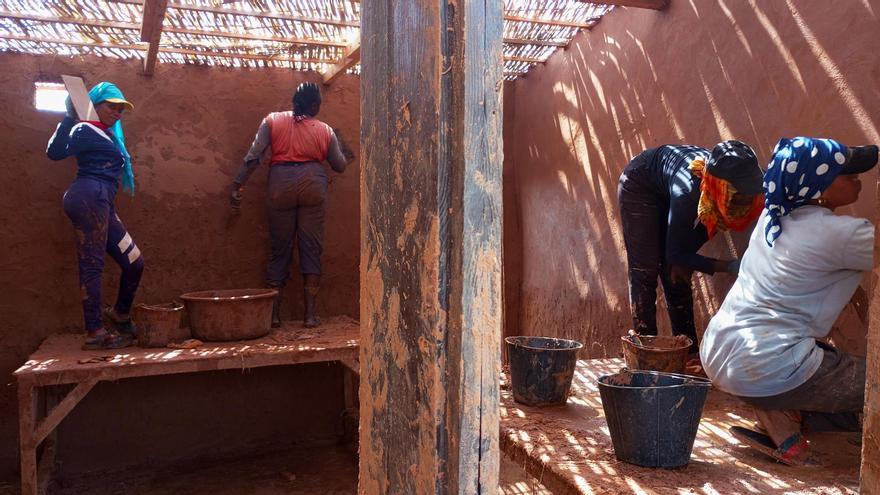 Unas mujeres aplican tierra en la pared para rehabilitar la residencia artística del centro de desarrollo comunitario Tabax Nité.